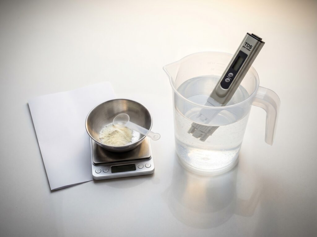 TDS pen measuring remineralized water in a pitcher next to a small scale for dosing powder